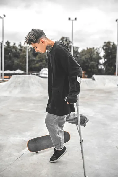 Guy with one leg on crutches near skateboard