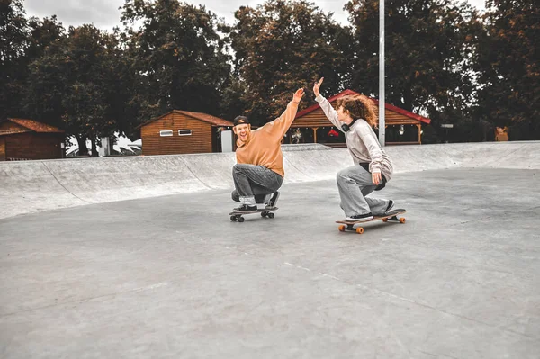 Guy et fille accroupi sur des planches à roulettes, levant la main avec bienveillance — Photo