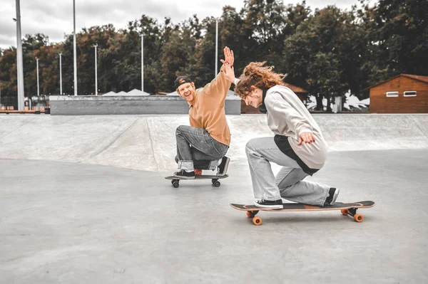 Chico y chica en patinetas estirándose el uno al otro — Foto de Stock