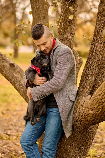 Un homme debout près de l'arbre avec un chien dans les mains — Photo