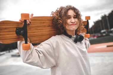 Omuzlarında kaykayla parkta duran bir kız.