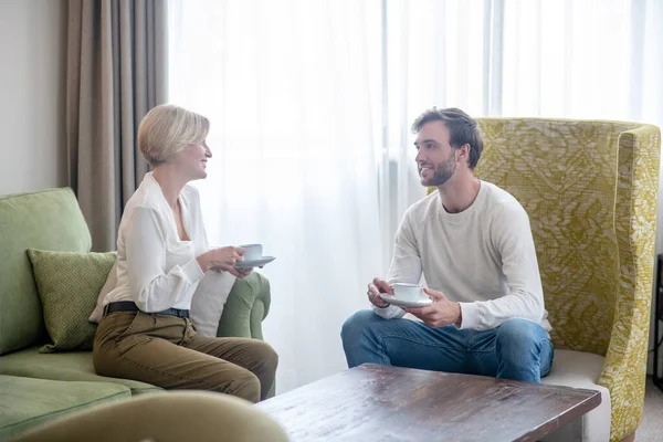 Blonde woman and her son sitting on the sofa and having tea — Stock Photo, Image