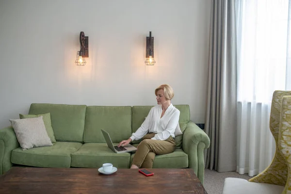 Mulher loira sentada em um sofá com um telefone nas mãos — Fotografia de Stock