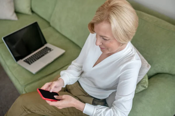 Szőke nő ül na kanapén egy telefon a kezében — Stock Fotó