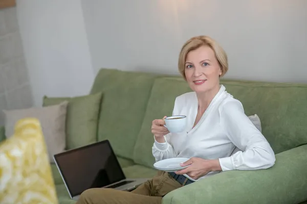 Donna bionda seduta sul divano e che prende il tè — Foto Stock