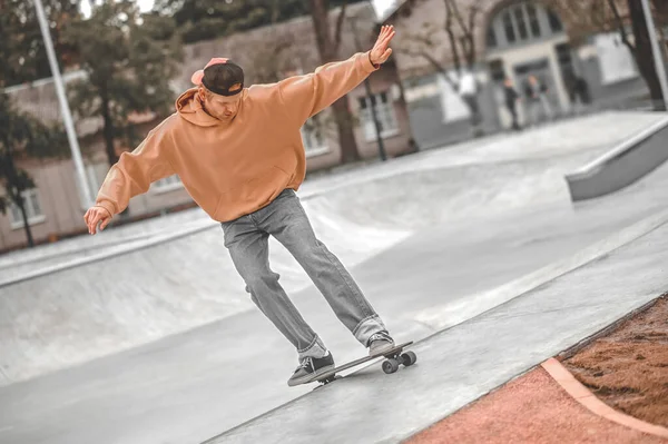 Facet z rękami na bokach jeżdżący na deskorolce w skateparku — Zdjęcie stockowe
