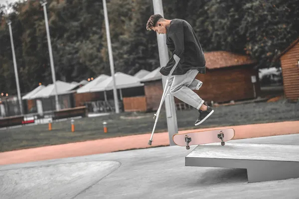 Kerl auf Krücken beim Sprung auf Skateboard vom Sprungbrett — Stockfoto
