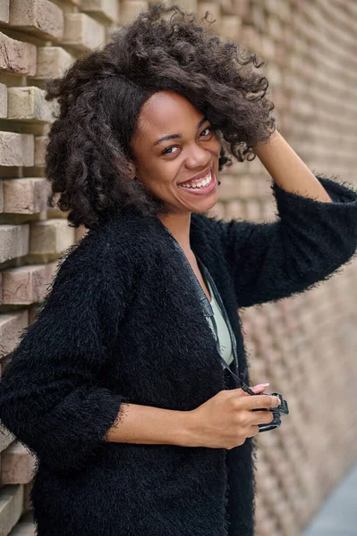 Smiling mulatta in black cardigan near the brick wall — Stock Photo, Image