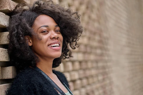 Smiling mulatta in black cardigan near the brick wall — Stock Photo, Image