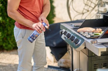 Kırmızı tişörtlü bir adam arka bahçede ızgara sebze pişiriyor.