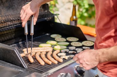 Izgara sosis ve sebze pişiren bir adam.