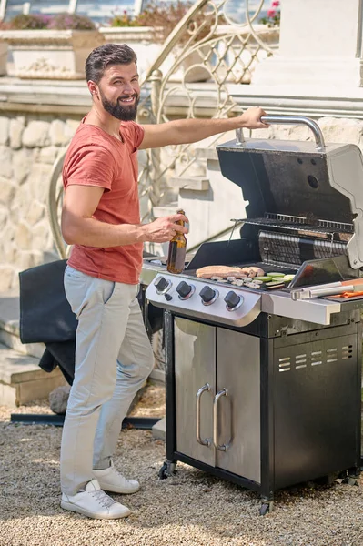 Um homem em uma camiseta vermelha cozinhar legumes grelhados no quintal — Fotografia de Stock