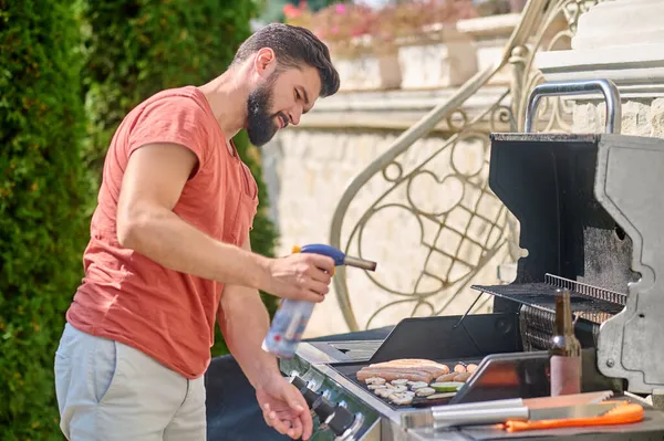 Um homem cozinhando salsichas grelhadas e legumes — Fotografia de Stock