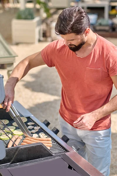 Muž vařící grilované klobásy a zeleninu — Stock fotografie