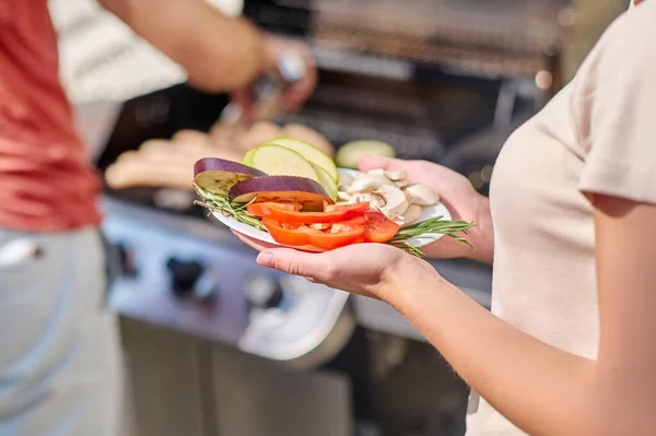 Een man in rood hemd staat bij de barbecue en kookt groenten — Stockfoto