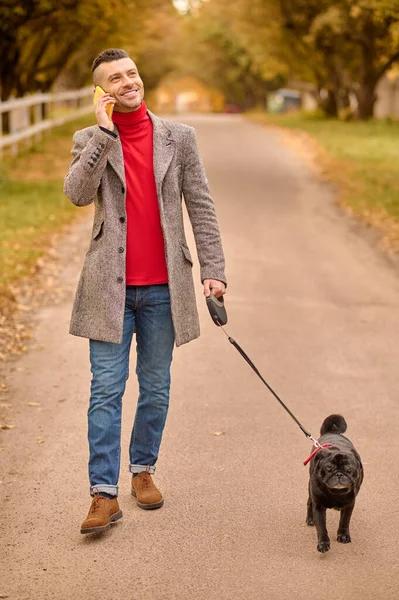 Homem tendo uma caminhada matinal com um cão e falando ao telefone — Fotografia de Stock