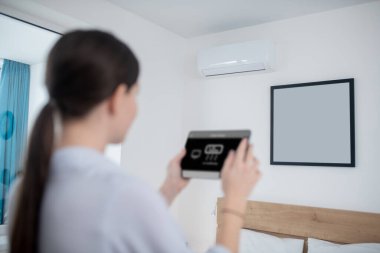 Kadın klimayı tablet kullanarak açıyor.