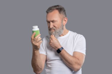 Elinde vitaminle kavanoz tutan sakallı bir adam.
