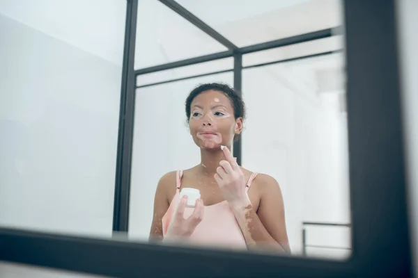 Eine süße junge Frau trägt Feuchtigkeitscreme auf ihr Gesicht auf — Stockfoto