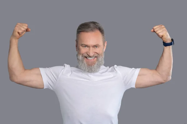 Ein reifer Mann im weißen T-Shirt zeigt seine Muskeln — Stockfoto