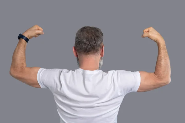 Ein reifer Mann im weißen T-Shirt zeigt seine Muskeln — Stockfoto