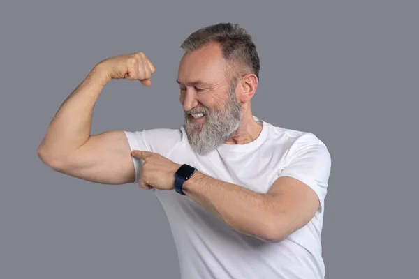 Dospělý muž v bílém tričku ukazující svaly — Stock fotografie