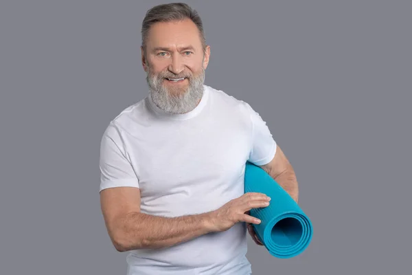 Homem barbudo segure um tapete para o treino — Fotografia de Stock