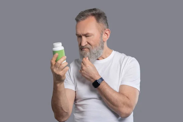 Um homem barbudo segurando um frasco com vitaminas — Fotografia de Stock