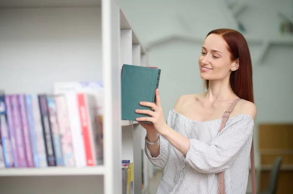 Mujer poniendo libro en estante en la biblioteca — Foto de Stock