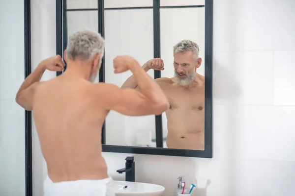 Hombre tensando los músculos de los brazos mirando en el espejo —  Fotos de Stock