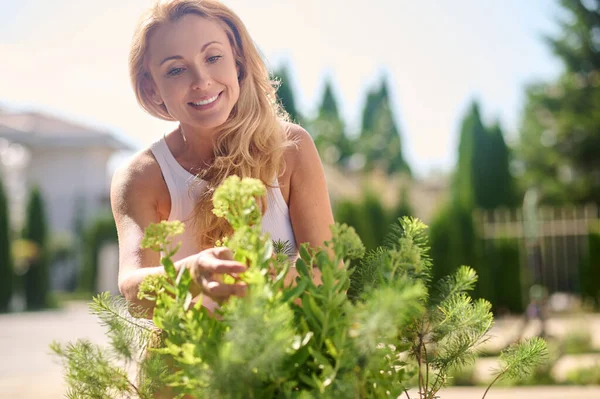 Jonge lachende vrouw in de tuin omgaan met bloemen — Stockfoto