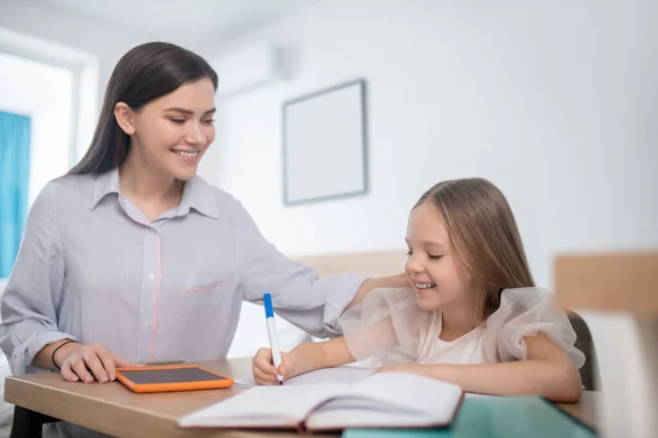 Radostná matka se dívá, jak její dcera dělá domácí úkoly — Stock fotografie