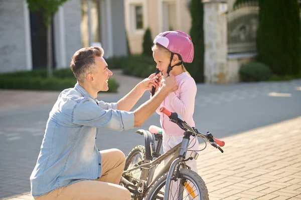 Un hombre que pone casco protector en la cabeza de sus hijas antes de montar en bicicleta — Foto de Stock