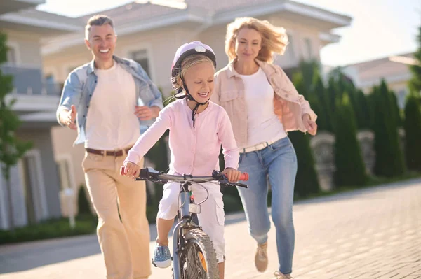 Una ragazza bionda carina che impara ad andare in bicicletta con i suoi genitori — Foto Stock