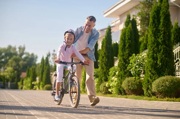 Papá montando una bicicleta con su hija sentada en ella — Foto de Stock