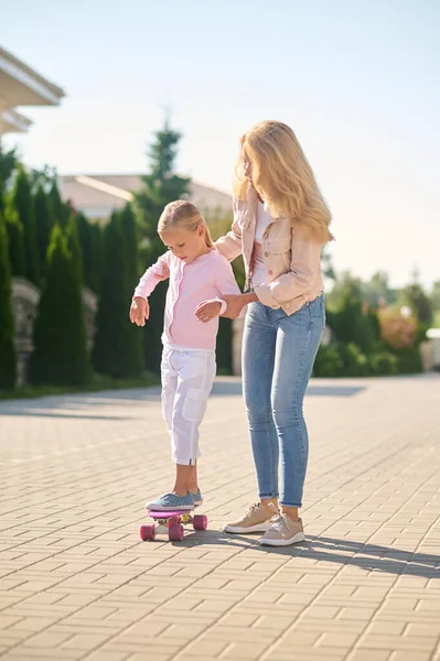 Mom helping her daughter ride a skateboard — Stock Photo, Image