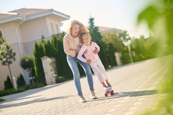 Mom helping her daughter ride a skateboard — Stock Photo, Image