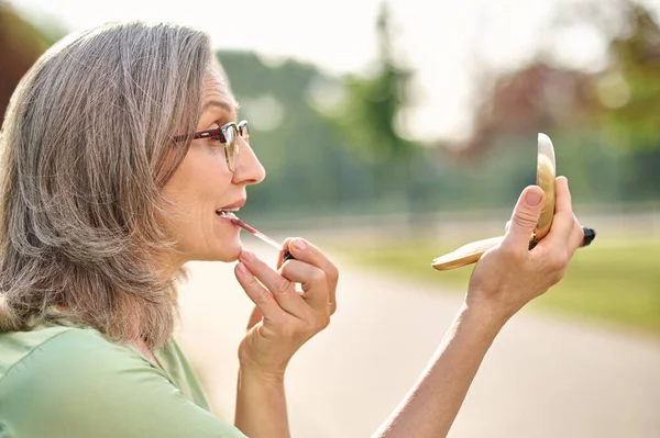 Perfil de mujer con gafas aplicar lápiz labial al aire libre — Foto de Stock