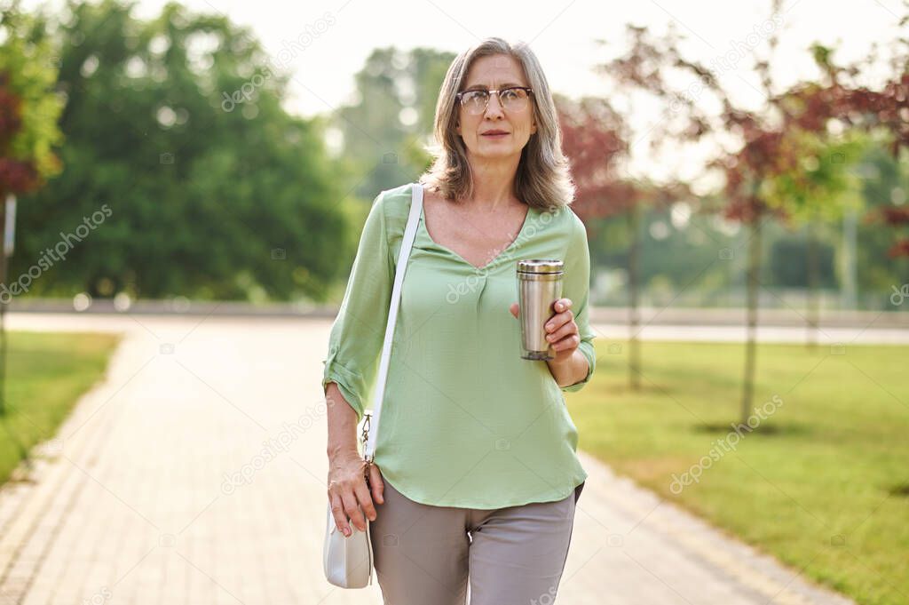 Woman holding drink walking in park
