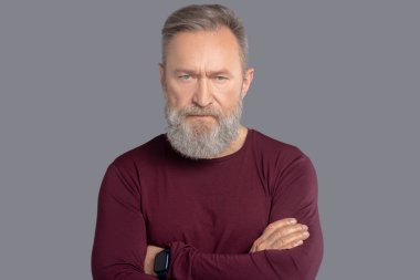 Burgonya gömlekli olgun bir adam ciddi görünüyor.