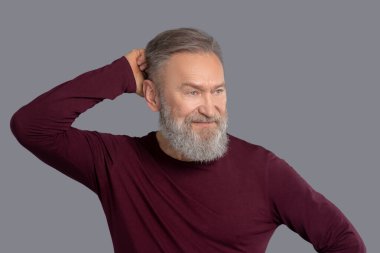 Burgonya gömlekli olgun bir adam belirsiz görünüyor.