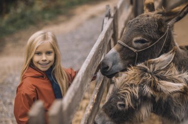 Sarışın bir kız sığır ağılının yanında duruyor donlarıyla ve gülümsüyor