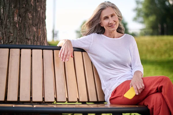 Женщина со смартфоном сидит на скамейке в парке — стоковое фото