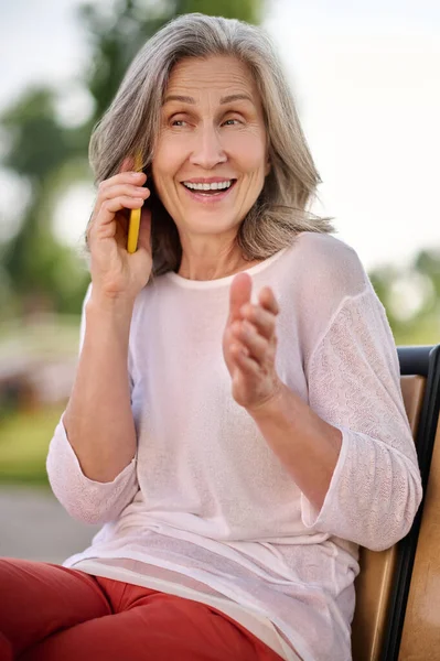 Женщина разговаривает на смартфоне улыбаясь жестом — стоковое фото