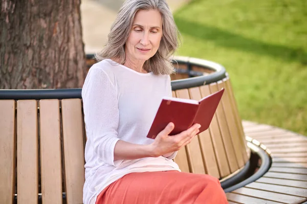 Kvinna läser boken sitter på bänken i parken — Stockfoto