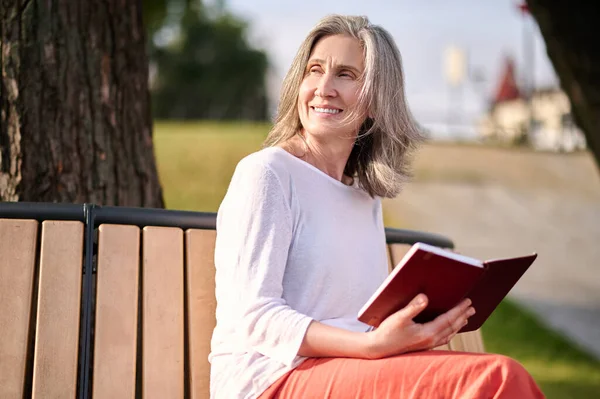 Mulher com livro sentado no parque olhando para o lado — Fotografia de Stock