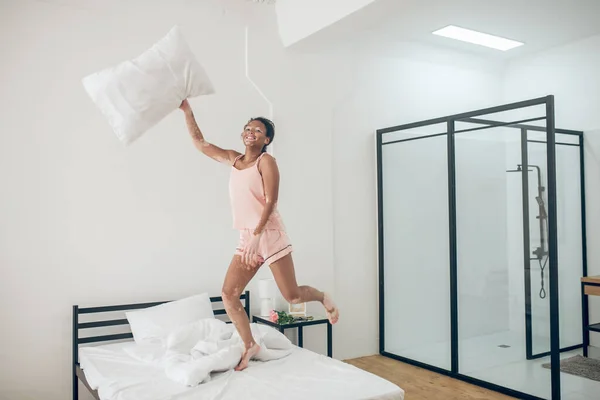 En ung kvinna i rosa underkläder hoppar i säng — Stockfoto