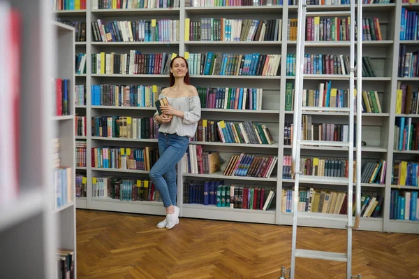 Kitapları tutan kadın kütüphanede yan yana bakıyor.