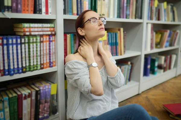 本棚の近くの床に座っている疲れた女性 — ストック写真