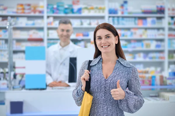 Длинноволосая женщина выглядит довольной после покупки товаров в аптеке — стоковое фото